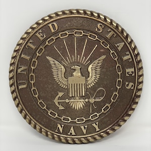 May include: A bronze-colored round plaque with a rope-like border. The center features a gold eagle with an anchor and a rope. The text "UNITED STATES NAVY" is inscribed around the border.