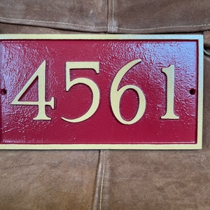 以下が含まれることがあります： 金色の縁取りと金色の文字で「4561」と書かれた赤い家の番号プレートです。