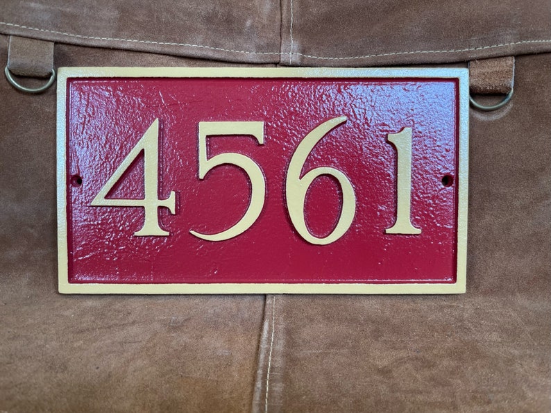 以下が含まれることがあります： 金色の縁取りと金色の文字で「4561」と書かれた赤い家の番号プレートです。
