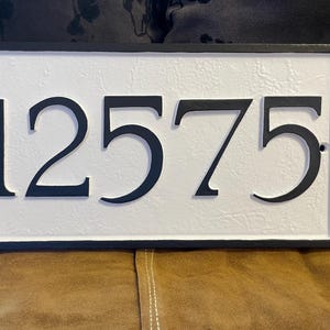 以下が含まれることがあります： 白地に黒で12575の数字が書かれた、黒と白の家の番号プレートです。