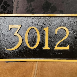 以下が含まれることがあります： 金色の縁取りと金色の文字で「3012」と書かれた黒い家の番号札