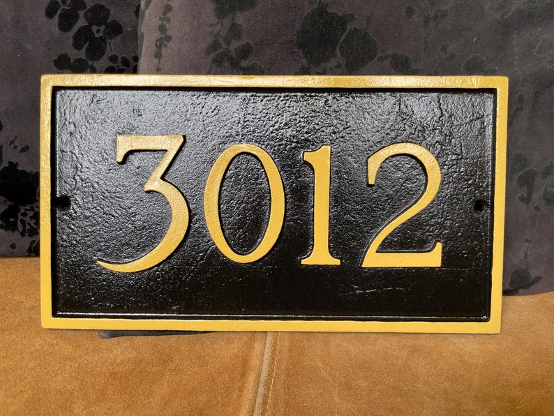 以下が含まれることがあります： 金色の縁取りと金色の文字で「3012」と書かれた黒い家の番号札