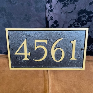以下が含まれることがあります： 金色の縁取りと金色の文字で「4561」と書かれた黒い家の番号プレート
