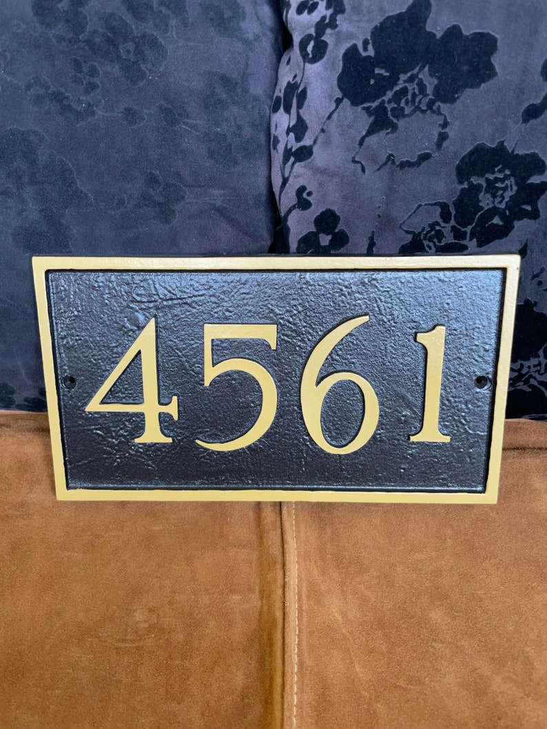 以下が含まれることがあります： 金色の縁取りと金色の文字で「4561」と書かれた黒い家の番号プレート