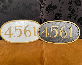 May include: Two oval-shaped house number signs with gold numbers on a white and black background. The numbers on both signs are 4561.