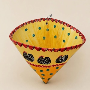 May include: A cone-shaped wall planter with a yellow base, featuring hand-painted black chickens with white polka dots, small teal floral accents, and a red scalloped border along the top rim. A small hole is present at the top for hanging.