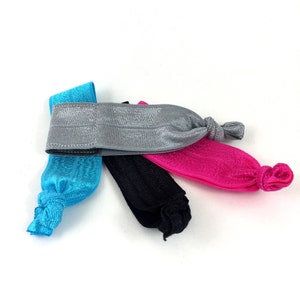May include: Four hair ties in different colors: turquoise, gray, black, and pink. The hair ties are made of a stretchy fabric and have a knotted design.