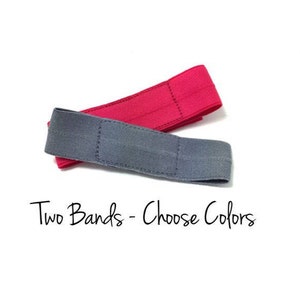 Op de afbeelding: Twee stoffen haarbandjes, een grijs en een roze.  "Two Bands - Choose Colors" staat onder de haarbandjes.