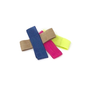 May include: Four fabric hair ties in different colors: brown, blue, pink, and yellow. The hair ties are arranged in a criss-cross pattern.