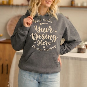 Może przedstawiać: Ciemnoszara melanżowa bluza z kapturem z przednią kieszenią typu kangurka oraz jasnokremowym napisem Real Model Yuor Desing Here Dream Mockup, ozdobiona małymi grafikami gwiazdek i zakrzywioną linią umieszczoną na klatce piersiowej.