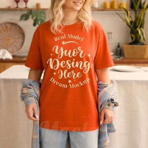 May include: A burnt orange short-sleeve t-shirt featuring white text that reads Real Model Yuor Desing Here Dream Mockup, arranged in a circular design with small stars, worn with a blue and white plaid flannel shirt tied around the waist.