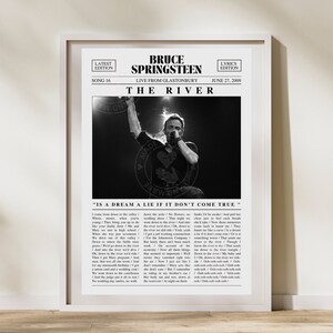May include: Black and white photo of Bruce Springsteen performing live at Glastonbury music festival. The image is a newspaper clipping with the headline "The River" and the song title "Is a Dream a Lie If It Don't Come True".
