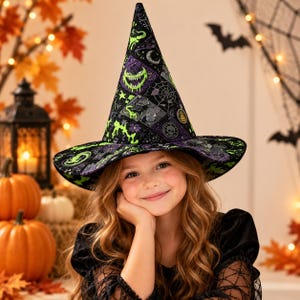 May include: A pointed witch hat featuring a black and purple quilted pattern with lime green graphic prints of grinning faces, spider webs, and skulls. The hat has a wide brim and a tall, conical crown with a dark, textured fabric finish.