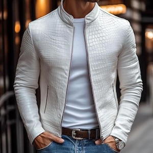 Puede incluir: Una chaqueta blanca con un patrón texturizado de piel de cocodrilo, cuello alto y cremallera frontal completa. La chaqueta se lleva sobre una camiseta blanca lisa, combinada con pantalones vaqueros azules y un cinturón de cuero marrón con hebilla.