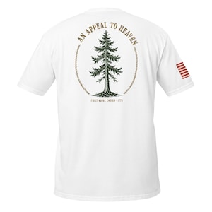 May include: A white short-sleeve t-shirt featuring a green pine tree graphic centred on the back, enclosed by a rope circle. The text AN APPEAL TO HEAVEN arches above, with FIRST NAVAL ENSIGN - 1775 below. A small red and white striped flag is on the sleeve.