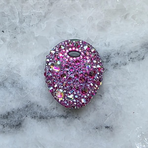 May include: A circular phone grip accessory featuring a dense, textured surface covered in numerous small, multifaceted pink and purple crystals. The design includes several iridescent heart-shaped accents integrated among the round stones.