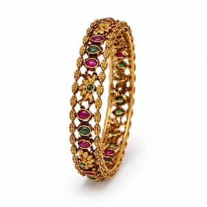 May include: A gold-toned bangle bracelet featuring an intricate openwork design with granulated metal textures. The piece is embellished with alternating marquise-shaped red and green stones, interspersed with small floral metal motifs.
