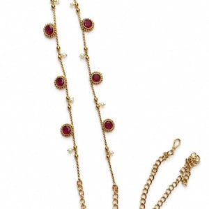May include: A long gold-tone chain necklace featuring evenly spaced circular red stones set in gold bezels, interspersed with small white beads. The necklace includes a sturdy link chain section at the bottom with a metal hook clasp closure.