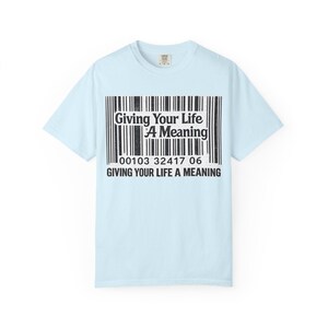 Op de afbeelding: Een lichtblauw t-shirt met korte mouwen en een zwart-witte streepjescode-afbeelding op de borst. De afbeelding bevat de tekst "Giving Your Life A Meaning" in het streepjescodegebied en nogmaals in dikke zwarte letters onder de cijfers.
