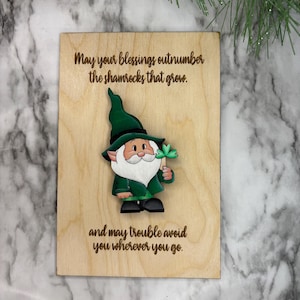 May include: A wooden card with a green leprechaun holding a four-leaf clover. The card reads "May your blessings outnumber the shamrocks that grow. And may trouble avoid you wherever you go."