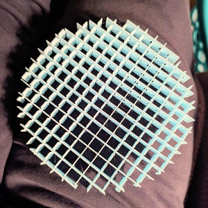 May include: A circular light blue grid structure featuring a series of intersecting vertical and horizontal walls that form a uniform square pattern across the entire surface, creating a geometric lattice design with open spaces between each divider.