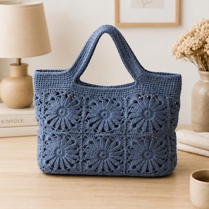 May include: A blue crochet tote bag constructed from six square panels featuring a raised floral or sunburst pattern. The bag has two integrated handles and a solid blue crocheted top border, showcasing a consistent yarn texture throughout.