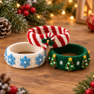 May include: Three circular crochet bracelets featuring holiday themes. One bracelet has red and white stripes with a candy cane accent. Another is cream-colored with blue snowflakes and small white beads. The third is dark green with small Christmas trees.