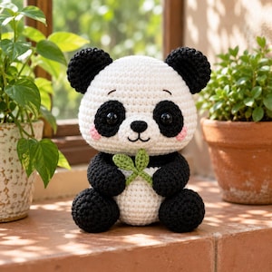May include: A crocheted panda toy featuring a white body and head with black ears, arms, legs, and eye patches. The panda has black safety eyes, a small black nose, a stitched mouth, and pink cheeks. It holds a small green crocheted leaf sprig.