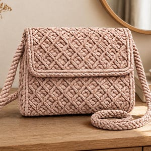 Può includere: Una borsa a tracolla color rosa polvere realizzata in corda spessa intrecciata, caratterizzata da una forma rettangolare strutturata con chiusura a patta. L'esterno presenta un motivo a rombi costante su tutto il corpo e la patta, completato da una spessa tracolla in corda abbinata.