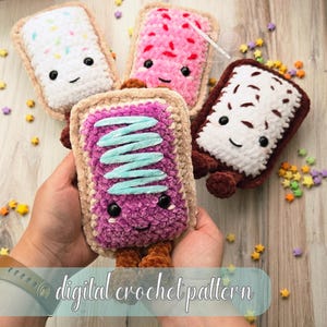 May include: Four plush, rectangular crochet toys resembling toaster pastries with embroidered smiling faces and black bead eyes. One is white with colorful sprinkles, one is pink, one is white with brown drizzle, and one is purple with blue icing.