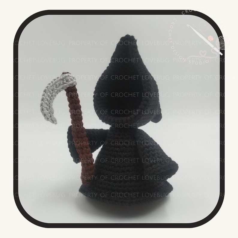 May include: A crocheted Grim Reaper doll with a black hooded robe and a gray scythe with a brown handle. The doll is handmade and has a whimsical design. The background is a light cream color.