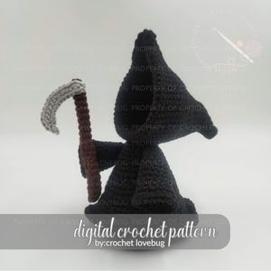 Könnte beinhalten: Gehäkelte Figur des Sensenmanns, in Schwarz, mit einer Sense. Die Sense hat eine graue Klinge und einen braunen Griff. Die Figur trägt einen Kapuzenmantel. Der Text "digital crochet pattern by: crochet lovebug" steht unten.