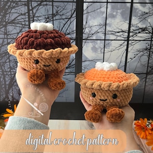 Peut inclure: Deux tartes en crochet avec des visages souriants, des yeux noirs et des joues roses. Une tarte a un dessus marron foncé et l'autre un dessus orange, toutes deux avec des touffes blanches et des croûtes marron. Texte digital crochet pattern.