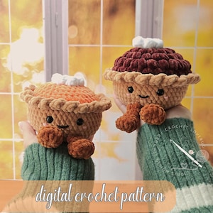 Op de afbeelding: Twee gehaakte pluche taartjes met lachende gezichtjes, zwarte ogen en roze wangen. Eén taartje is oranje met een beige korst, de andere is donkerbruin met een beige korst. Beide hebben witte toefjes bovenop en kleine bruine voetjes.