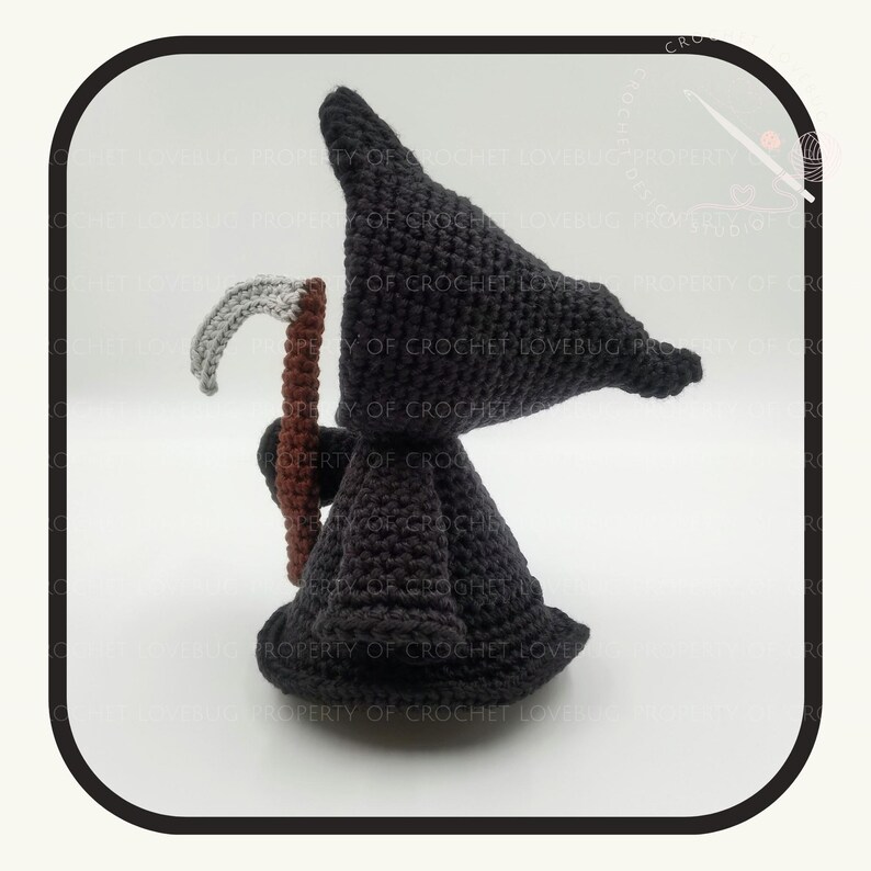 May include: A crocheted figure of the Grim Reaper, featuring a black hooded cloak and a scythe. The scythe has a gray blade and a brown handle. The figure is handmade and stands on a white surface.