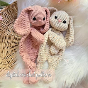 May include: Two handmade crochet bunny dolls in soft pink and cream colors. The bunnies have long floppy ears, button eyes, and pink noses. The text "digital crochet pattern" is written across the bottom of the image.