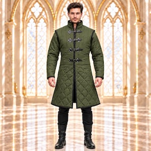 Può includere: Un lungo cappotto trapuntato verde oliva con collo alto, bordi neri e quattro cinturini in pelle frontali con fibbie in metallo. L'indumento presenta maniche lunghe e un motivo a losanghe trapuntato su tutta la superficie fino alle cosce.