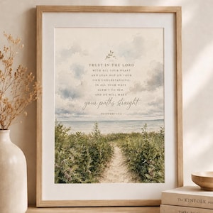 Op de afbeelding: Een ingelijste kunstdruk met een aquarellandschap van een zandpad dat door groene duinen naar de oceaan leidt onder een bewolkte lucht. De tekst luidt: TRUST IN THE LORD WITH ALL YOUR HEART AND LEAN NOT ON YOUR OWN UNDERSTANDING; IN ALL YOUR WAYS SUBMIT TO HIM, AND HE WILL MAKE your paths straight. PROVERBS 3:5-6.