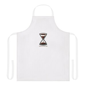 May include: A white apron featuring a central graphic of a coffee dripper shaped like an hourglass, with dark brown coffee liquid dripping into the base. Below the graphic, the text SLOW EXTRACTION is printed in a simple, dark, sans-serif font.