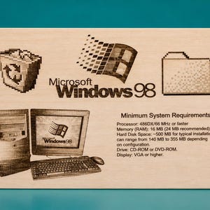 May include: A rectangular light-coloured wooden plaque featuring a laser-engraved Microsoft Windows 98 logo, a recycle bin icon, a folder icon, a desktop computer illustration, and the text Minimum System Requirements with technical specifications.