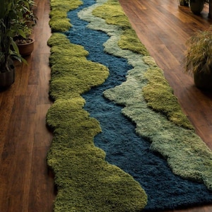 Könnte beinhalten: Ein langer, rechteckiger Läufer mit einer texturierten, getufteten Oberfläche, die eine gewundene Flusslandschaft nachahmt. Das Design kombiniert tiefe Blautöne in der Mitte mit verschiedenen Schattierungen von Moosgrün und Salbeigrün.