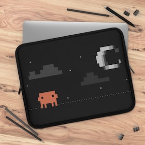 May include: A black laptop sleeve featuring a pixelated graphic of a crescent moon, two dark gray clouds, small white stars, and an orange square-shaped character on a dotted line. The sleeve has a black zipper and a rectangular shape.