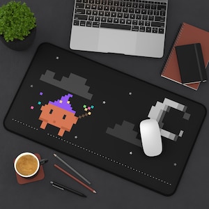 May include: A rectangular black desk mat featuring a pixel art design of an orange creature wearing a purple wizard hat, holding a wand with colorful sparkles, set against a night sky with a crescent moon, clouds, and small white stars.