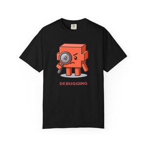 May include: A black short-sleeve t-shirt featuring a graphic of a square orange character holding a magnifying glass to its eye. The character has a serious expression, and the word DEBUGGING is printed in red capital letters below it.