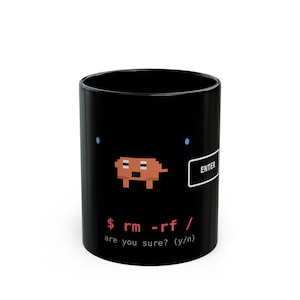 May include: A black ceramic mug featuring a pixelated brown dog graphic, a white rectangular button labeled ENTER, and red command line text that reads $ rm -rf / followed by the white text are you sure? (y/n) on the front surface.