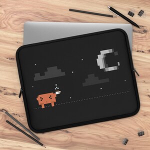 May include: A black laptop sleeve featuring a pixel art design of an orange creature standing on a dotted line under a night sky. The scene includes dark gray pixelated clouds, a white crescent moon, and small white stars against the black background.