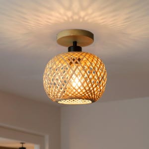 May include: A flush mount ceiling light fitting featuring a spherical shade crafted from woven light brown bamboo strips. The fitting includes a circular wooden base and a black metal connector, casting a patterned light onto the ceiling.