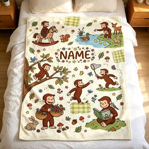May include: A cream-colored fleece blanket featuring a repeating pattern of brown monkeys in various activities, including riding a rocking horse, reading a book, and picking berries. The center includes the text NAME surrounded by floral accents.