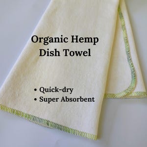 May include: A white organic hemp dish towel with green stitching. The towel is folded in half and has the text "Organic Hemp Dish Towel" and "Quick-dry Super Absorbent" printed on it.