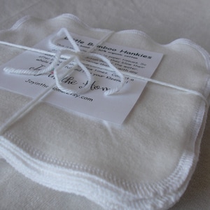 May include: A stack of white, soft, bamboo hankies with scalloped edges. The hankies are tied together with a white string and a small white tag with the text "Little Bamboo Hankies 30% organic cotton This is made to paper tissues. So often they blow their nose with any water. Sew times. Contact a Joyinthe homersy.com"